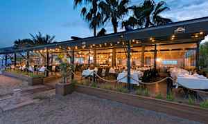 En restaurang vid stranden med vita dukar på kvällstid. (AI-genererad text)