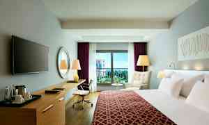 Ett modernt hotellrum med en säng, skrivbord, fåtölj och balkong med utsikt. (AI-genererad text)