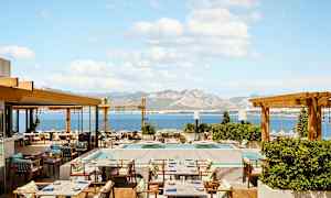 En restaurangterrass med havsutsikt och berg i bakgrunden. (AI-genererad text)