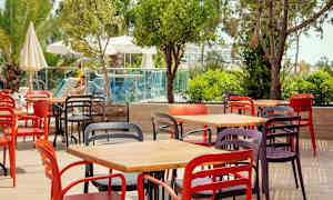 Färgglada stolar och bord placerade på en utomhusterrass nära grönska och en pool. (AI-genererad text)