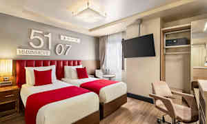 Två enkelsängar med röda sängkläder i ett modernt hotellrum. (AI-genererad text)