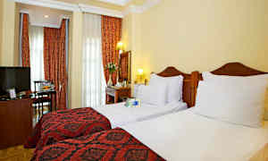 Hotellrum med två enkelbäddar, röda dekorationer och gardiner. (AI-genererad text)