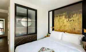 Hotellrum med en stor säng, tidningar på sängen och en dekorativ vägg. (AI-genererad text)