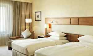 Ett hotellrum med två enkelsängar, en sittplats med kudde och ett fönster med draperier. (AI-genererad text)