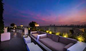 En takterrass med soffor och sittplatser, upplyst under en färgstark kvällshimmel. (AI-genererad text)