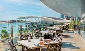 Uteservering med dukade bord och havsutsikt. (AI-genererad text)