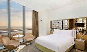 Bild av ett hotellrum med stor säng, två stolar, bord och fönster med utsikt. (AI-genererad text)