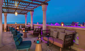 En överbyggd terrass med sittmöbler och belysning, med utsikt över havet på kvällen. (AI-genererad text)