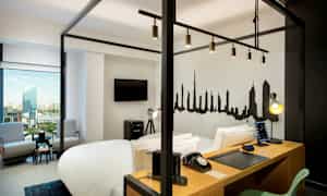 Ett modernt hotellrum med en himmelsäng, arbetsbord, TV, sittgrupp och en stadssiluett målad på väggen. (AI-genererad text)