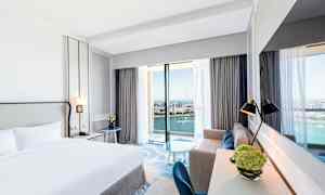 Hotellrum med dubbelsäng och havsutsikt genom stora fönster. (AI-genererad text)