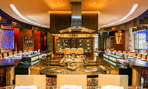 Interiör av en restaurang med öppen kökslayout och sittplatser runt. (AI-genererad text)