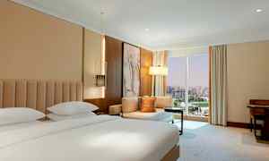 Ett hotellrum med en dubbelsäng, sittgrupp och ett stort fönster med stadsutsikt. (AI-genererad text)