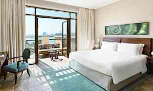 Modernt hotellrum med en stor king size-säng, en sittgrupp och öppen balkong med havsutsikt. (AI-genererad text)