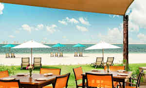 En strandutsikt med solstolar under parasoll och ett matbord med stolar i förgrunden. (AI-genererad text)