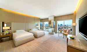 Två enkelsängar i ett modernt hotellrum med stora fönster och stadsvy. (AI-genererad text)