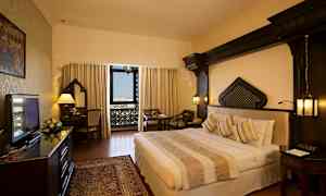 Ett hotellrum med en dubbel säng, skrivbord och sittgrupp. Fönstret har utsikt med dekorativa detaljer. (AI-genererad text)