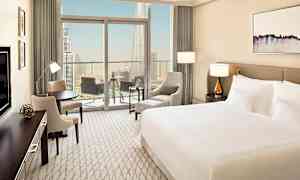 Ett modernt hotellrum med en stor säng, sittgrupp och en balkong med utsikt över en stor stad. (AI-genererad text)