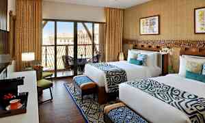 Två bäddade sängar i ett hotellrum med modern inredning, stora fönster med balkong och utsikt. (AI-genererad text)