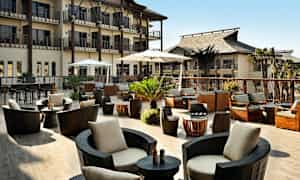 En utomhusterrass med moderna sittplatser, parasoller och växter, omgiven av byggnader. (AI-genererad text)