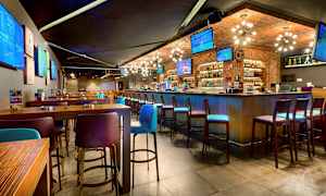 Interiör av en modern bar med höga bord och stolar samt flera TV-skärmar på väggarna. (AI-genererad text)