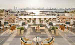 En utomhusterrass med möbler och utsikt över en hamn och stadssilhuett i bakgrunden. (AI-genererad text)