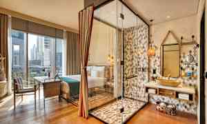 Ett hotellrum med stora fönster. Ett duschområde med glasväggar syns bredvid en tvättställ och spegel. (AI-genererad text)