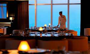 En restaurang med elegant dukade bord och stora fönster som vetter mot en utsikt. (AI-genererad text)