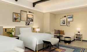 Ett hotellrum med två sängar, soffa och dekorativa målningar på väggen. (AI-genererad text)