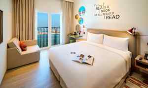 Ett hotellrum med en stor säng, sittplats, och öppet fönster med utsikt över havet. (AI-genererad text)