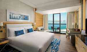 Hotelrum med dubbelsäng, sittgrupp och balkong som har utsikt över havet. (AI-genererad text)