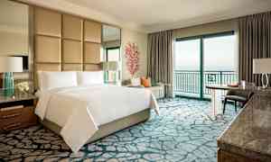 Ett lyxigt hotellrum med dubbelsäng, sittgrupp och havsutsikt. (AI-genererad text)