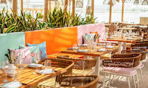 En uteservering med dukade bord, färgglada kuddar och grönska. (AI-genererad text)