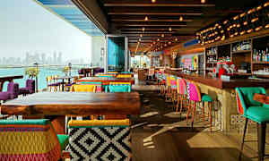 En modern restaurang med färgglada stolar och barstolar, trämöbler och utsikt över en stadssiluett vid vattnet. (AI-genererad text)