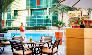 Ett cafébord med två drycker och en bakelse vid en pool, omgiven av träd och en glasvägg. (AI-genererad text)