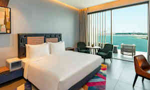 Ett modernt hotellrum med en stor säng, sittmöbler och ett stort fönster med utsikt över havet. (AI-genererad text)