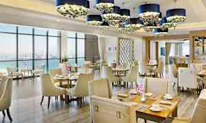 Interiör av en elegant restaurang med havsutsikt, ljusa möbler och dekorativa ljuskronor. (AI-genererad text)