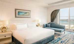 Ett hotellrum med en stor säng och en blå soffa, fönster med utsikt mot havet. (AI-genererad text)
