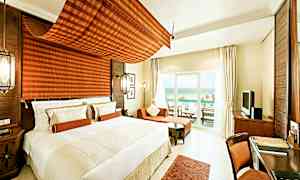 Ett modernt och ljust hotellrum med en stor säng, sittområde och en möblerad balkong som vetter mot havet. (AI-genererad text)