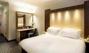 Ett hotellrum med en stor säng, en arbetsyta med stol och en spegel. (AI-genererad text)