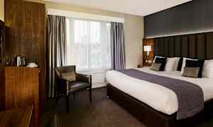 Ett hotellrum med stor säng, fåtölj och träinredda detaljer. (AI-genererad text)