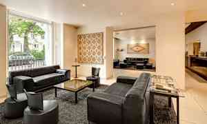 Ett elegant hotellrum med svarta soffor och fåtöljer, ett bord i mitten och konstverk på väggarna. (AI-genererad text)