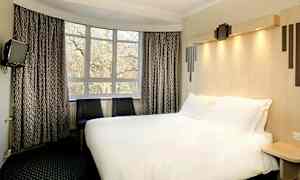 Ett hotellrum med en stor säng, två stolar och ett fönster med trädutsikt. (AI-genererad text)