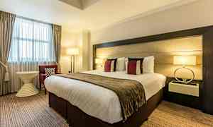 Ett hotellrum med en stor säng, dekorativa kuddar, lampor och möbler. (AI-genererad text)