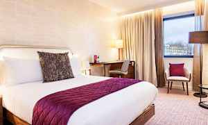 Ett hotellrum med en dubbelsäng, ett skrivbord och en stol, bredvid ett fönster. (AI-genererad text)