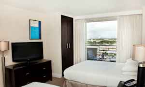 Ett hotellrum med två sängar, en tv på en byrå, en garderob och en balkong med utsikt. (AI-genererad text)