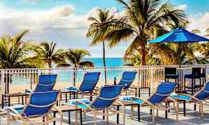 Soldäck med blå solstolar och parasoll framför en strand och palmer. (AI-genererad text)