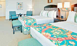 Hotellrum med två sängar, dekorerade med färgglada överkast. I rummet finns också en sittgrupp med två stolar och ett bord samt väggdekorationer. (AI-genererad text)