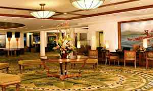 Ett elegant hotellobby med dekorativa mattor, en central blombukett och bekväma sittmöbler. (AI-genererad text)