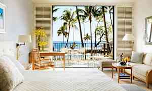 Hotellrum med ljus inredning, en säng, en sittgrupp och en balkong med utsikt över havet och palmträd. (AI-genererad text)