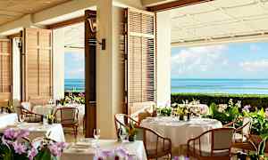 En restaurang med bord dukade med vita dukar och blommor. Bakgrunden visar havsutsikt med blå himmel. (AI-genererad text)